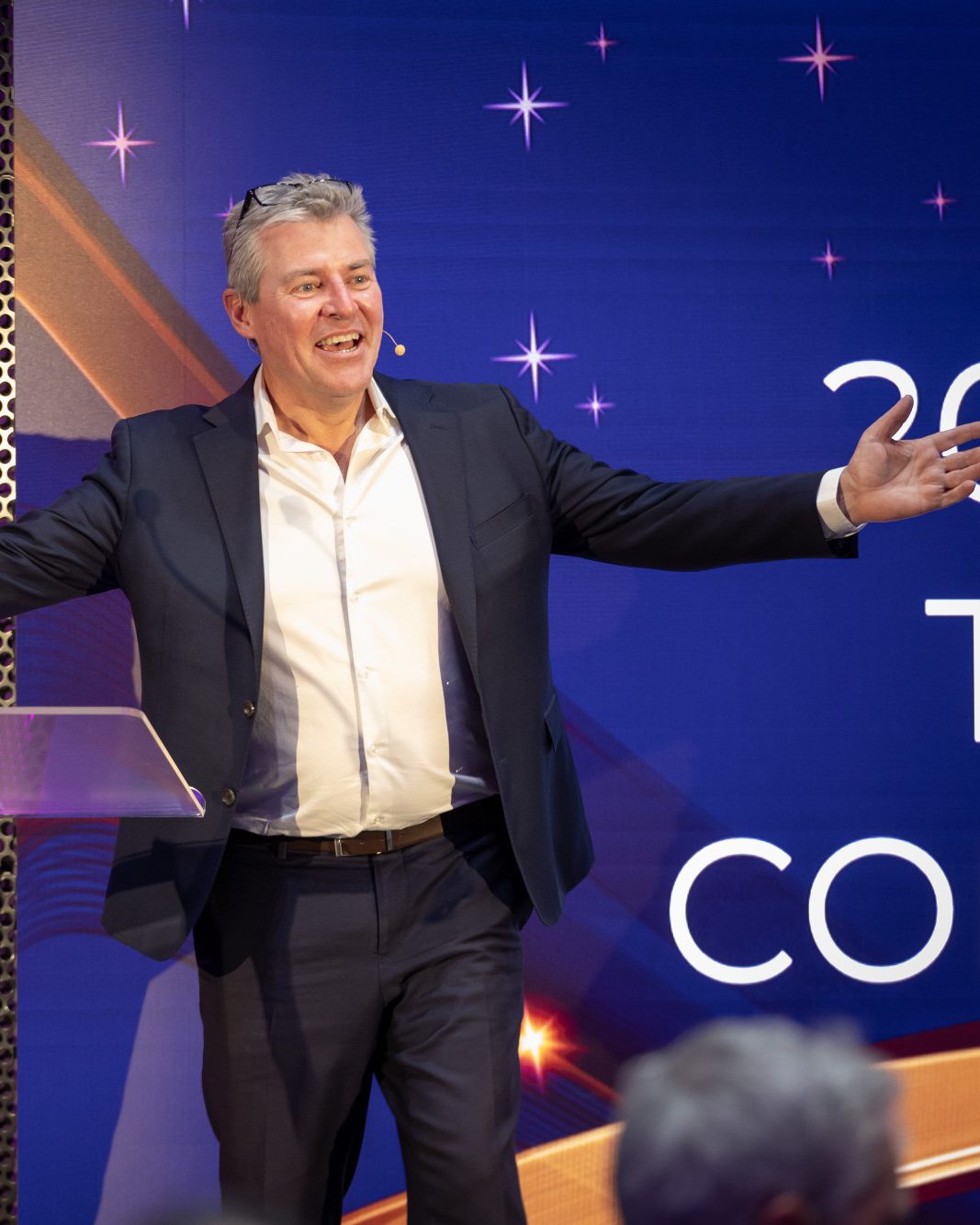 Michael Teulon on stage, arms wide, hosting an awards night